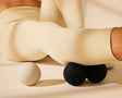 Trainer sitting using black massage balls on right calf